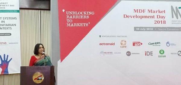 A woman in a red sari delivering a speech at a market-based resilience building event in Bangladesh.