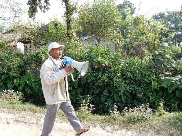 A man with a megaphone walking down a dirt road, facing challenges and lessons from early warning systems in reaching the last mile.