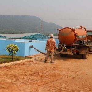 A man is standing next to a blue truck pioneering waste treatment in Odisha, India.