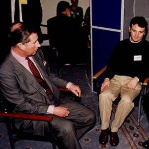 Three men celebrate Happy Birthday HRH The Prince of Wales while sitting in chairs talking to each other.