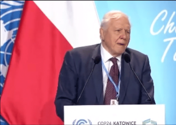 A man in a suit discussing the future of Climate Change at a podium.