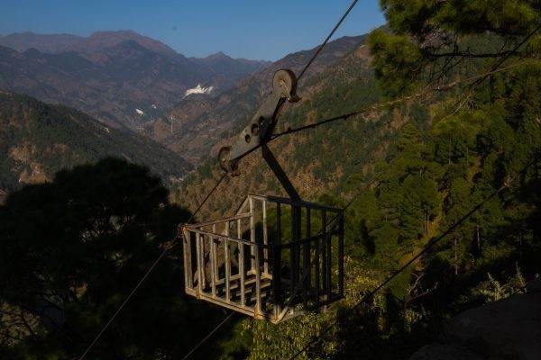 A gravity-powered cable car traversing through mountainous terrain with a scenic backdrop of trees.