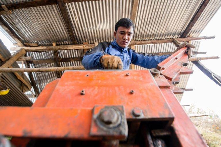 A man in a blue shirt is working on rebuilding settlements using a machine for moulding bricks.