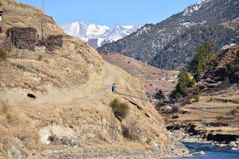 A man is starting small, walking down a hill in Karnali next to a river.