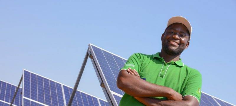 A man in a green shirt standing in front of sustainable energy solar panels.