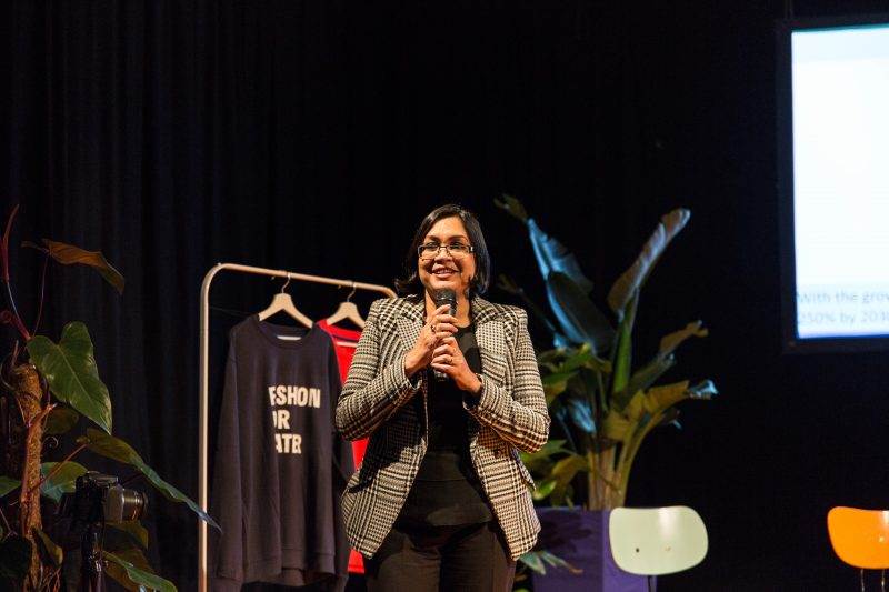 A woman, captivatingly fashion-forward, speaking into a microphone on stage.
