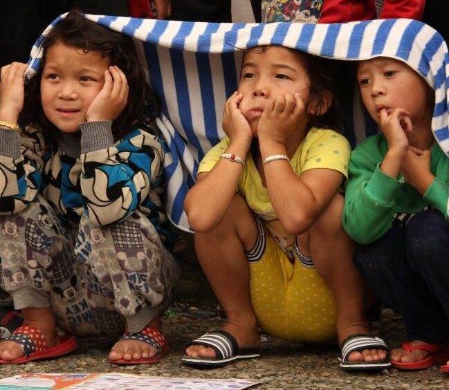 A group of children participating in the Nepal Reconstruction Campaign sit under a blanket.