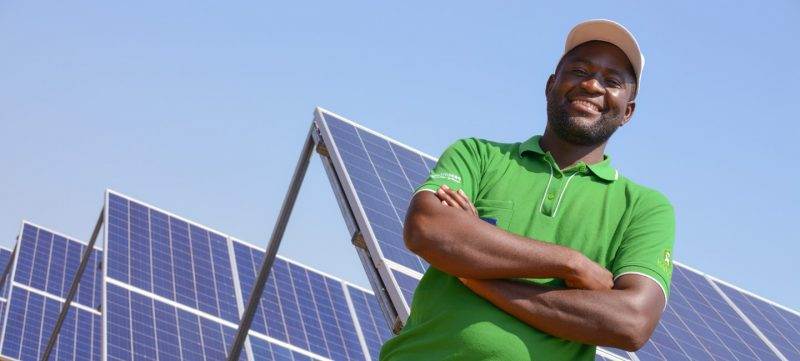A man in a green shirt stands in front of solar panels, showcasing the incredible energy transformation.