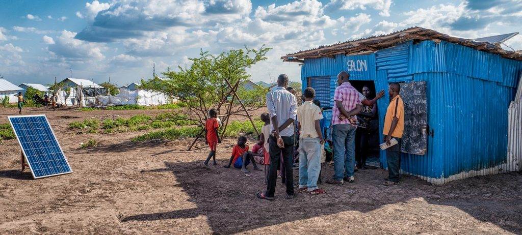 A group of Our People standing in front of a blue shack