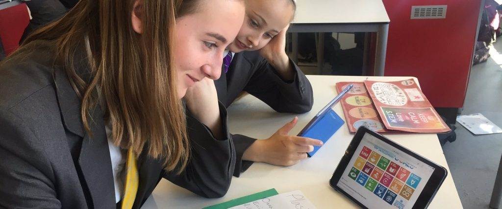 Two girls engage in a plastics challenge while sitting at a table with an iPad.