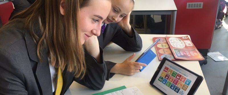 Two girls engage in a plastics challenge while sitting at a table with an iPad.