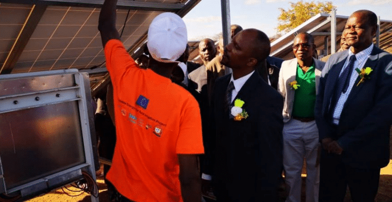 A group of men standing in front of a solar panel, inspiring Zimbabwe.