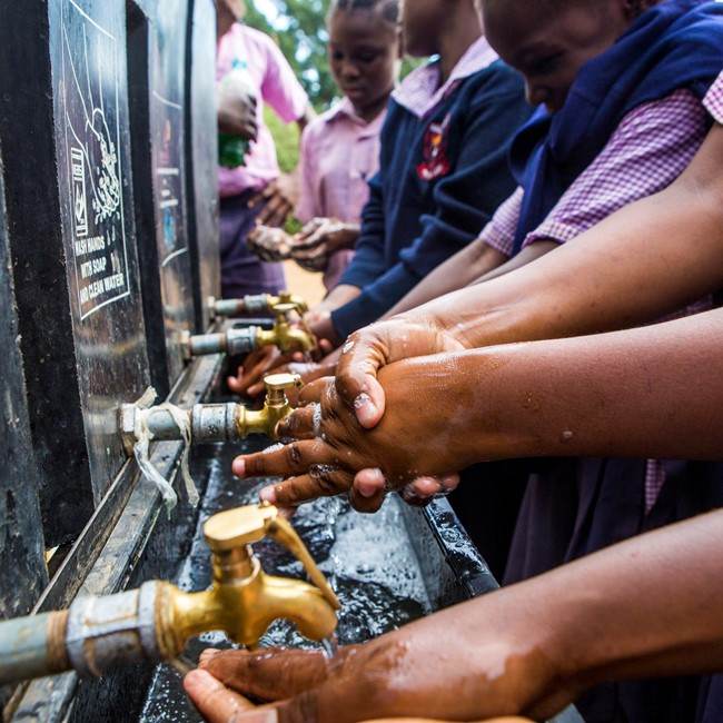 A group of school children getting involved in hygiene by washing their hands at a water fountain.