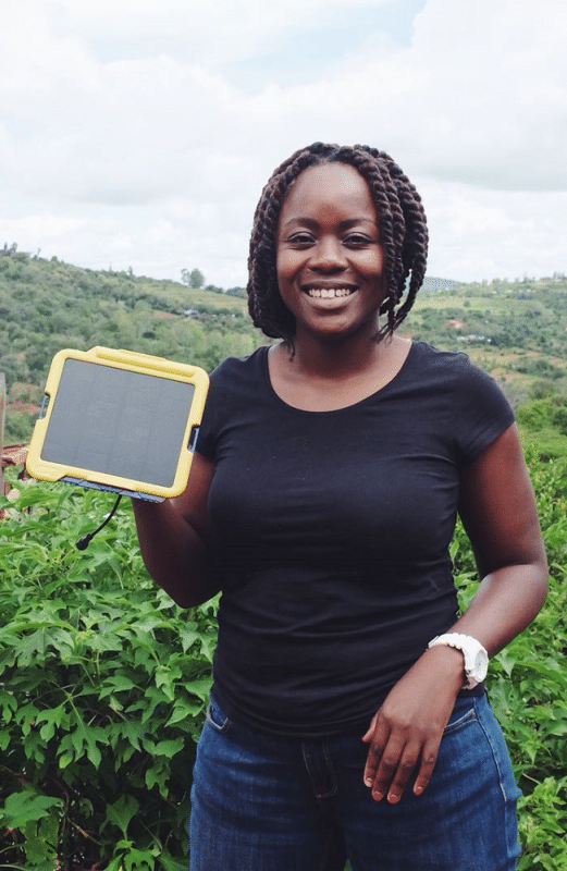A woman holding a solar panel in a field, representing the global push for renewable energy.