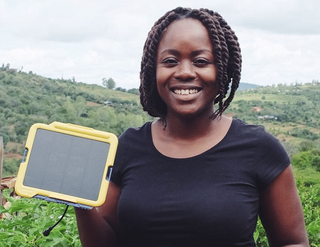 A woman holding a solar panel in a field, representing the global push for renewable energy.