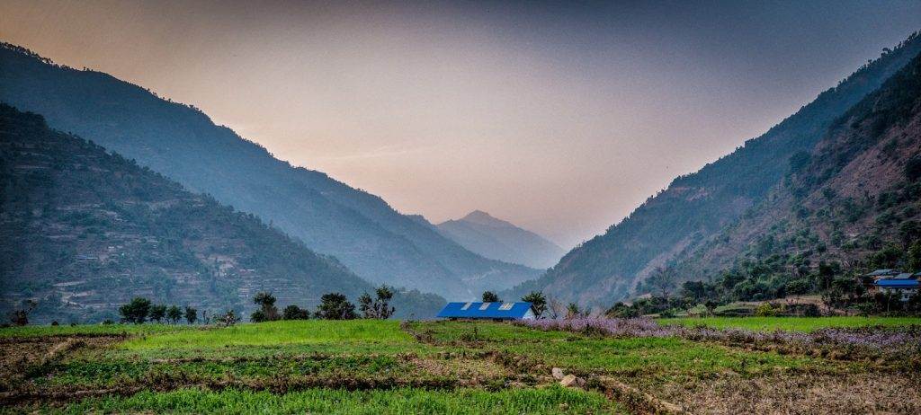 A house situated within a secluded field amidst mountainous terrain, highlighted in the context of Poor People's Energy Outlook (PPEO).