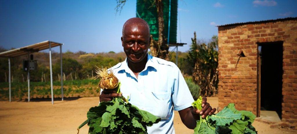 A man holding a bunch of vegetables in front of a house.