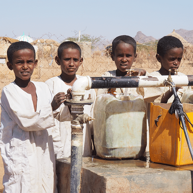A group of boys making water work at a pump.