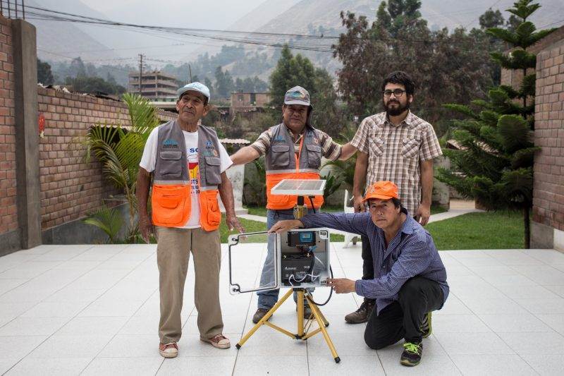 Four men posing with a landslides resilience device in front of a building.