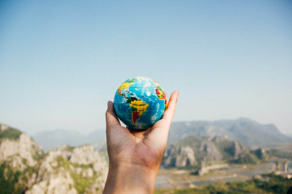 Design for a better world poster featuring a hand holding a globe with mountains in the background.