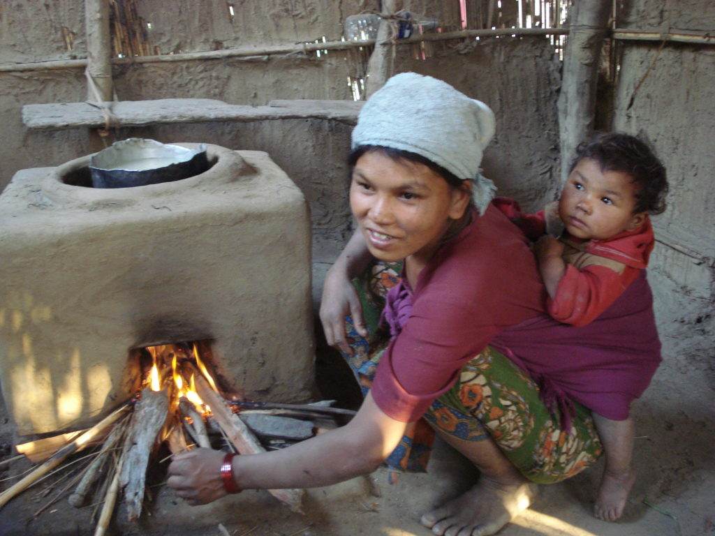 A woman holding a child keeping warm in front of a smoky fire in their home.