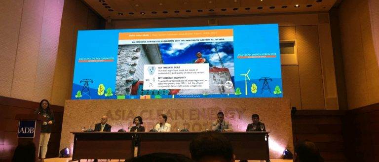 A group of people sitting on a stage in front of a large screen discussing impactful partnerships for inclusive energy access at scale.