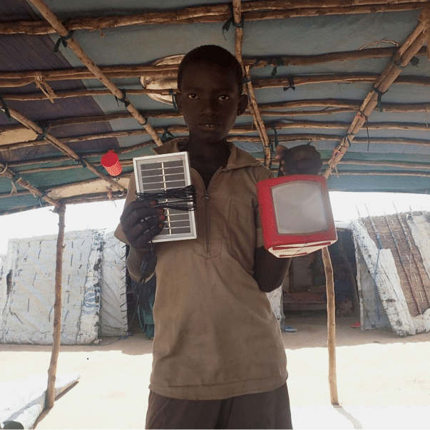 A boy showcasing a solar-powered TV, providing light and power for refugees in Burkina Faso.