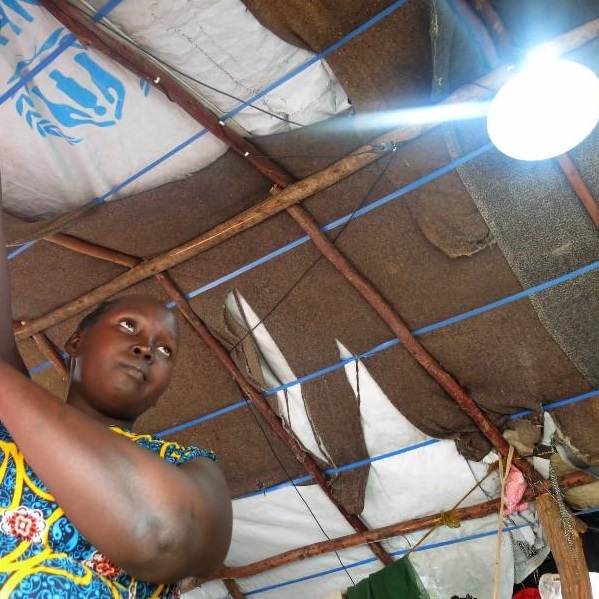 A woman is installing a light fixture in a hut to provide power for refugees in Burkina Faso.