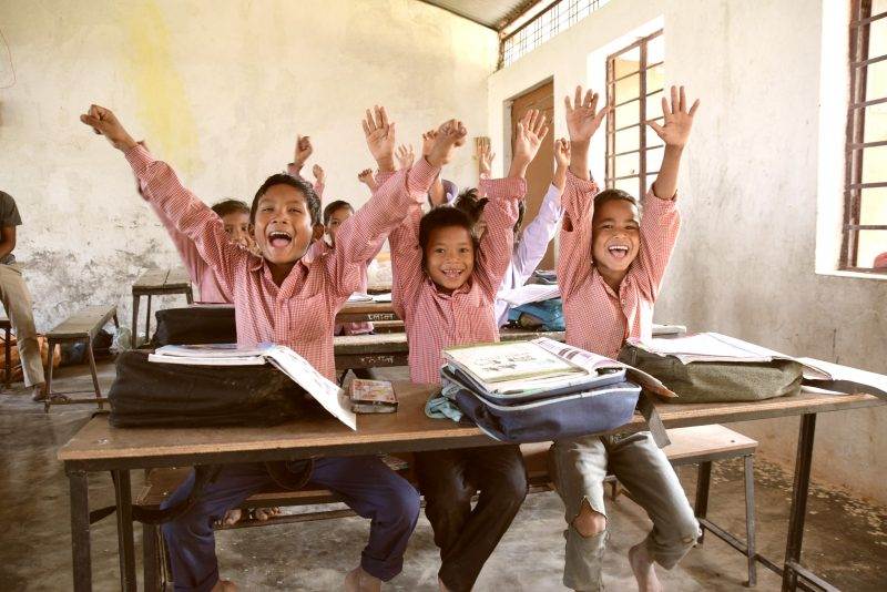 A classroom of children raising their hands, empowered by your support.