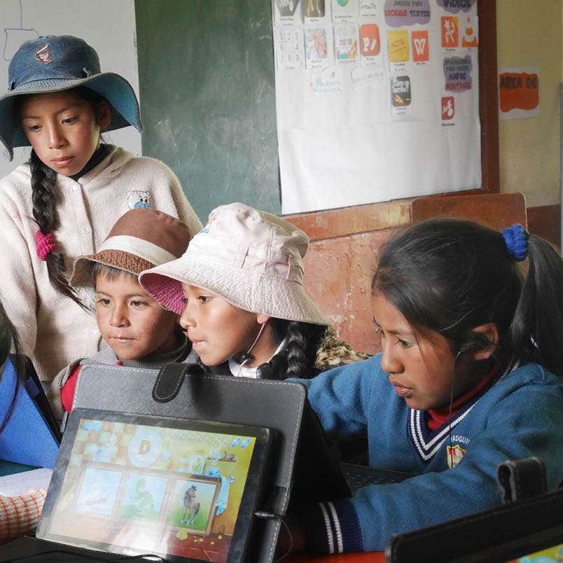 A group of energetic children huddled around a table, excitedly using an e-gifted tablet computer.