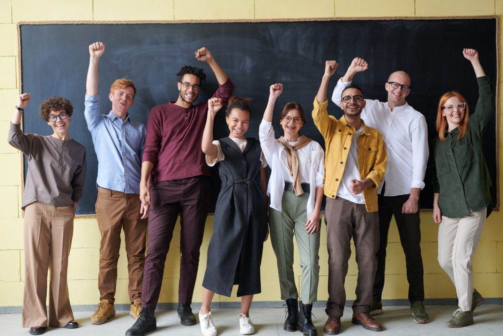 A group of people lined up in front of a chalkboard, raising their fists.