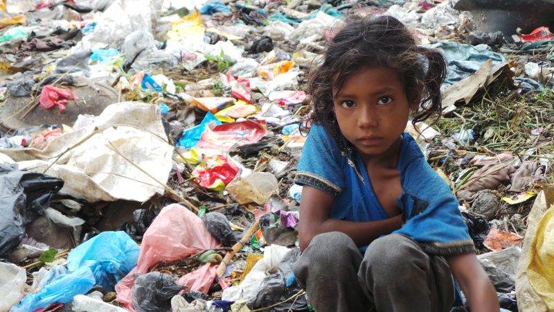A young girl sitting in front of a pile of garbage, exploring if 'frontier technologies' can aid the urban poor's critical issues.