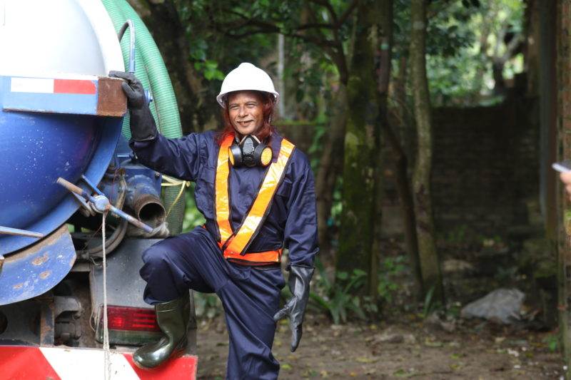 A man in a hard hat standing next to a garbage truck, emphasizing World Toilet Day 2019.