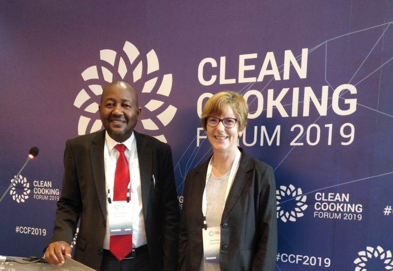 Two people advocate for clean cooking in front of a sign.