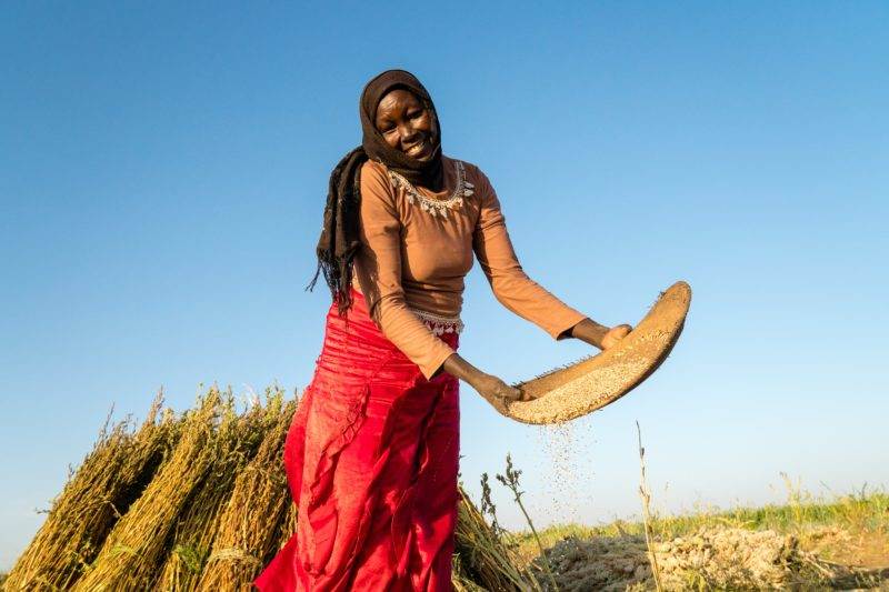 A woman is facing the new climate reality with practical action, standing in front of a pile of wheat.
