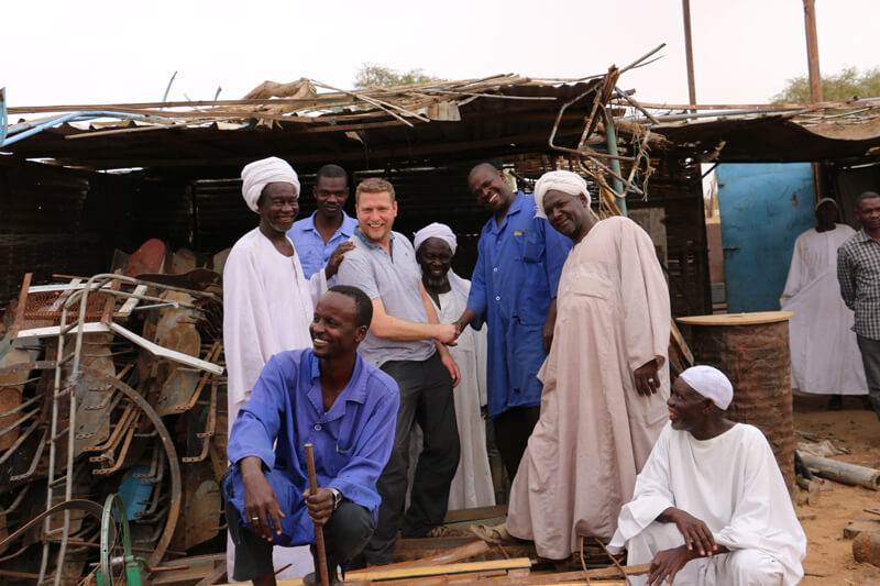 A group of men standing in front of PART 1 – DARFUR'S NEW DISCO DESTINATION shack.
