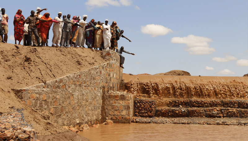 A group of people directing and controlling water flow at a dam edge.