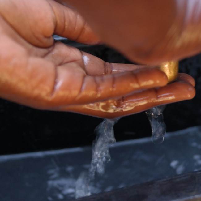 A person's hand is being washed with water from a tap.
