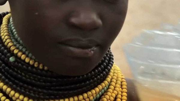A young girl wearing a necklace made of beads participates in water and sanitation videos.