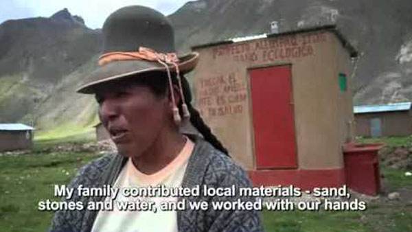 A woman in a hat is standing in front of a house, featured in water and sanitation videos.