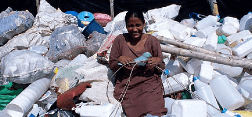 A woman surrounded by a pile of plastic bottles in a recycling center.