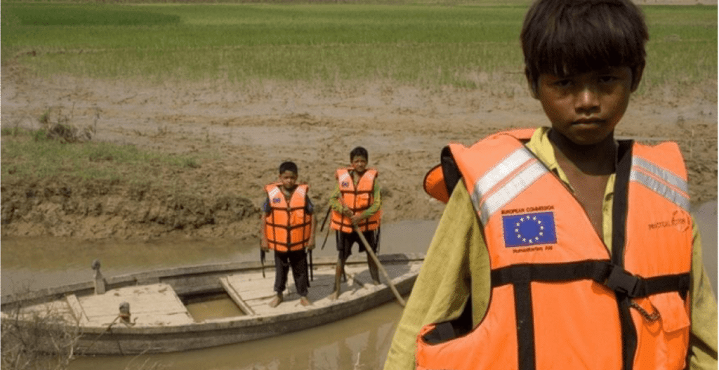 A group of children in life jackets standing on a boat in a muddy area.