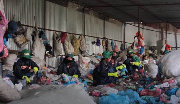 A group of people are sitting in a warehouse full of plastics challenge.