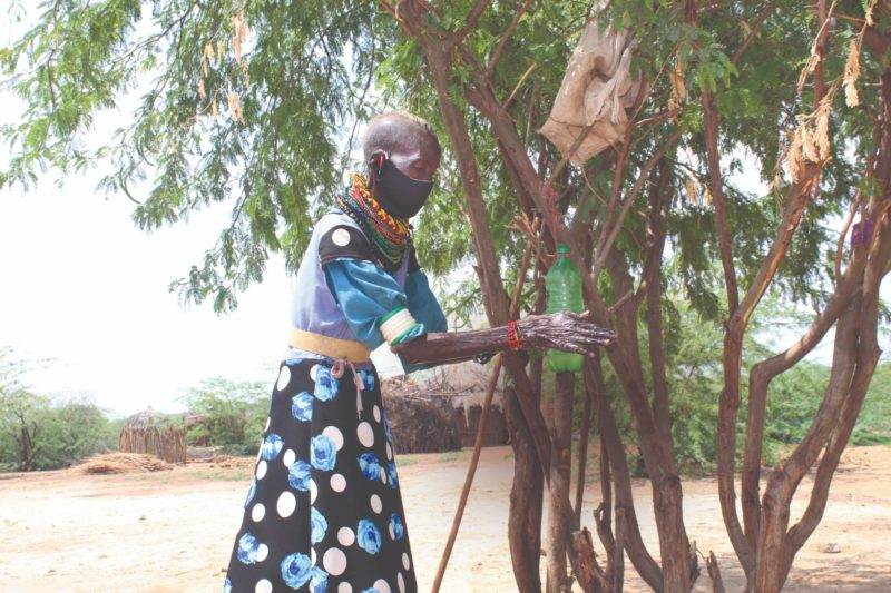 A woman, masked, stands near a tree.