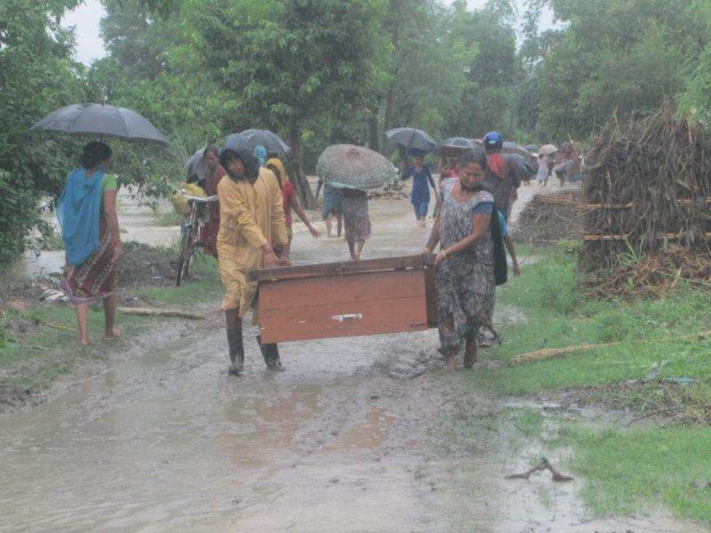 A group of people carrying a box down a muddy road while preparing for floods to prevent disaster.