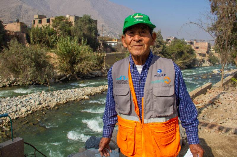 A resilient old man standing next to a river, protected by time.