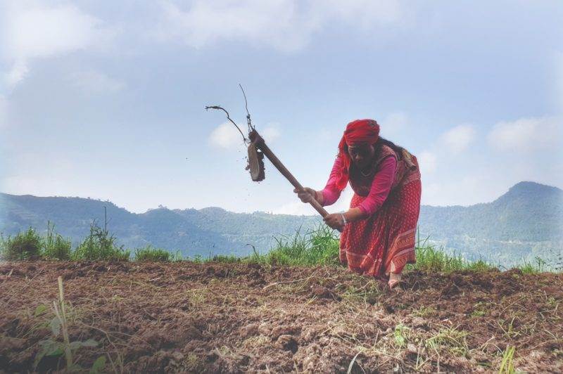 A woman utilizes a special feature to plow a field with a shovel.