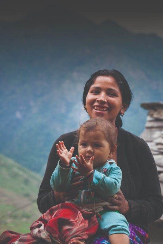 A woman holding a child with special feature clothing in front of mountains.