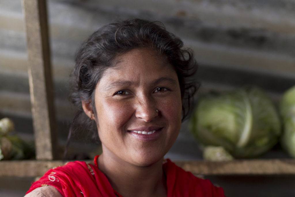 A woman ​utilizing​ business skills while smiling in front of cabbages.