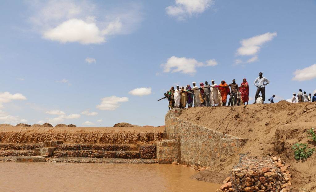 A group of people standing near a body of water, promoting a donation upgrade.